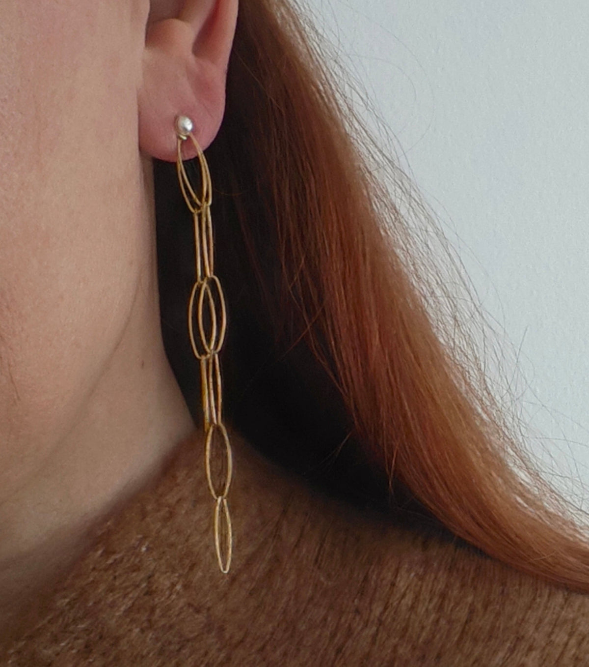 Gold chain earring worn by a person with light skin and brown hair.