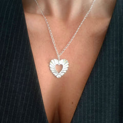 Woman wearing Phos Heart necklace in sterling silver, open heart pendant with radiant texture.