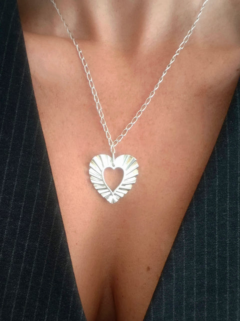 Woman wearing Phos Heart necklace in sterling silver, open heart pendant with radiant texture.