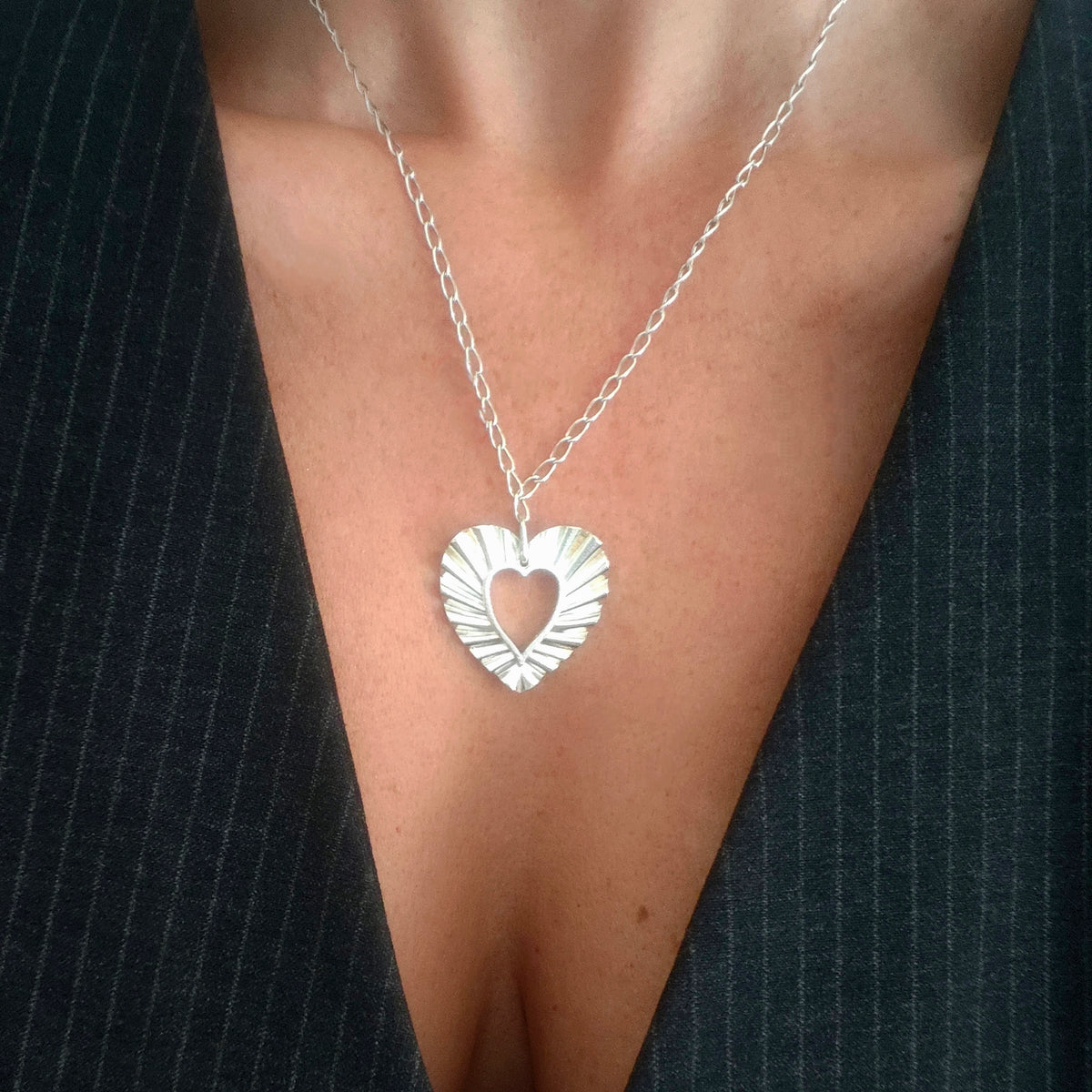 Woman wearing Phos Heart necklace in sterling silver, open heart pendant with radiant texture.