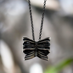 Silver bow-shaped pendant on a chain against a blurred natural background