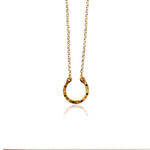 Gold horseshoe pendant necklace by Athenart, featuring black zircons and a delicate gold chain, inspired by traditional good luck symbols.
