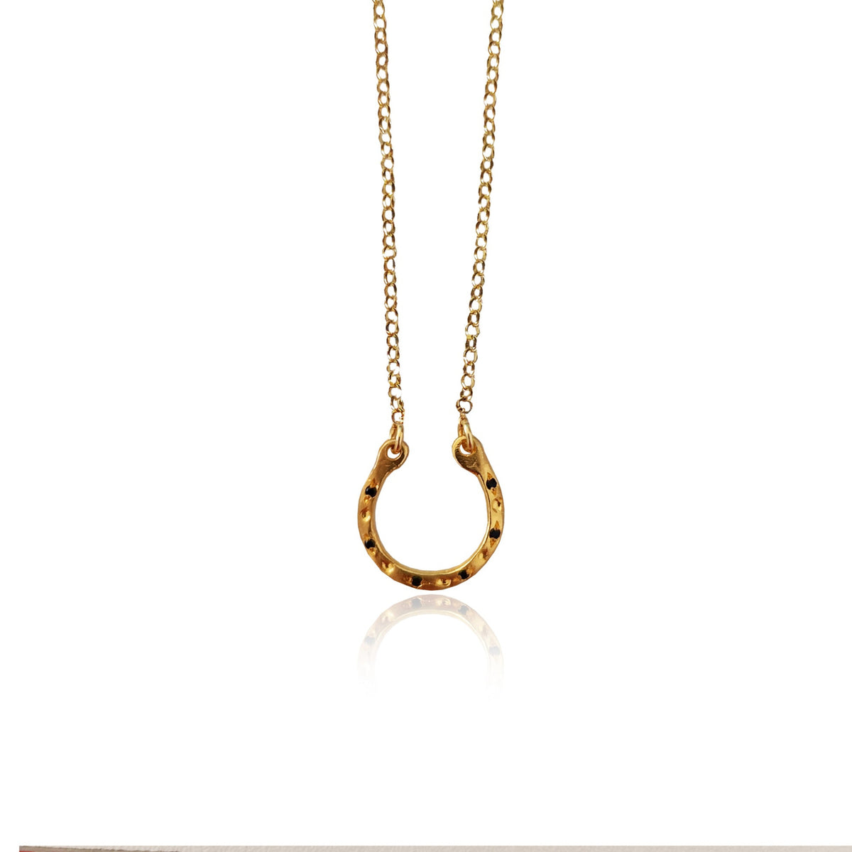 Gold horseshoe pendant necklace by Athenart, featuring black zircons and a delicate gold chain, inspired by traditional good luck symbols.