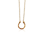 Gold horseshoe pendant necklace by Athenart, featuring red zircons and a delicate gold chain, inspired by traditional good luck symbols.