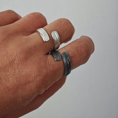 Hand wearing multiple silver rings on a plain background