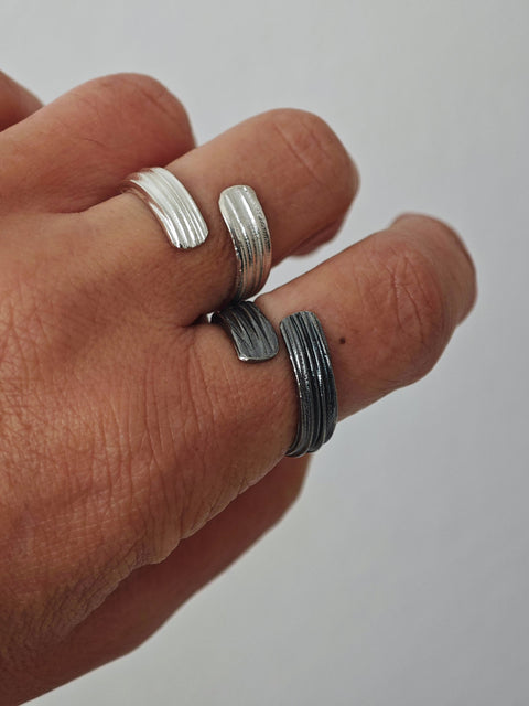 Hand wearing multiple silver rings on a plain background