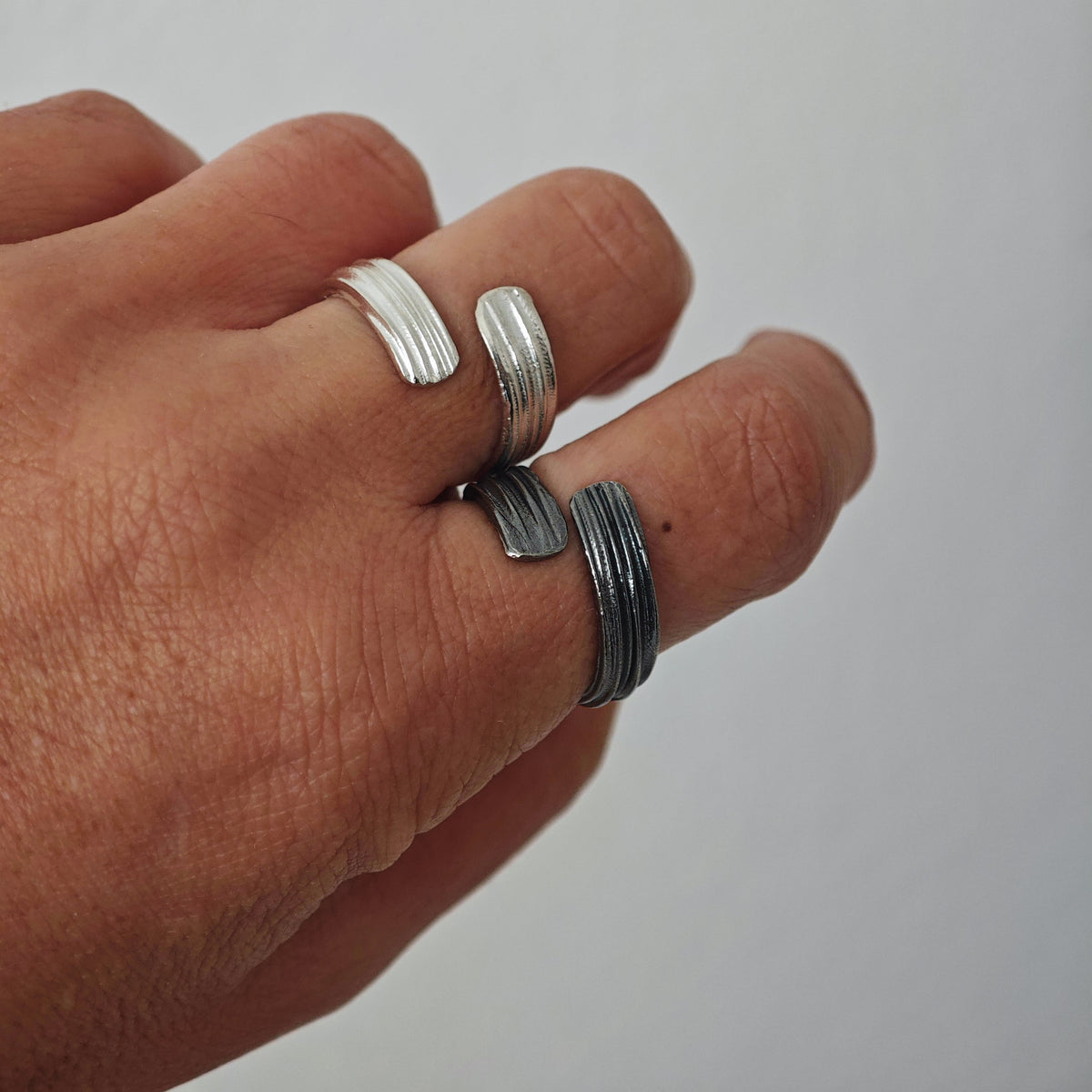 Hand wearing multiple silver rings on a plain background