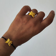 Hand wearing a gold butterfly ring with matching bracelet on a plain background