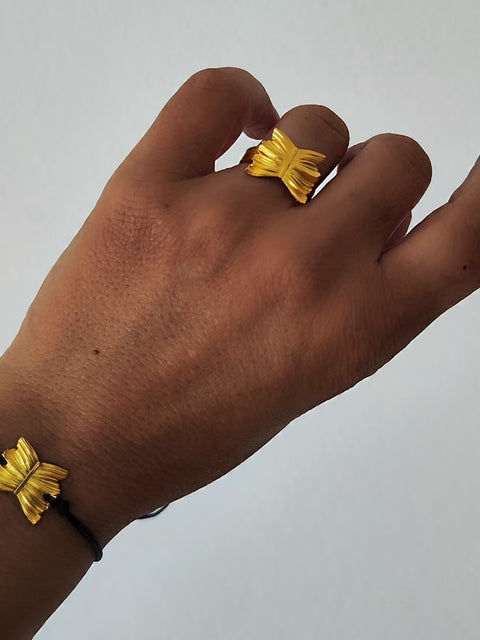 Hand wearing a gold butterfly ring with matching bracelet on a plain background