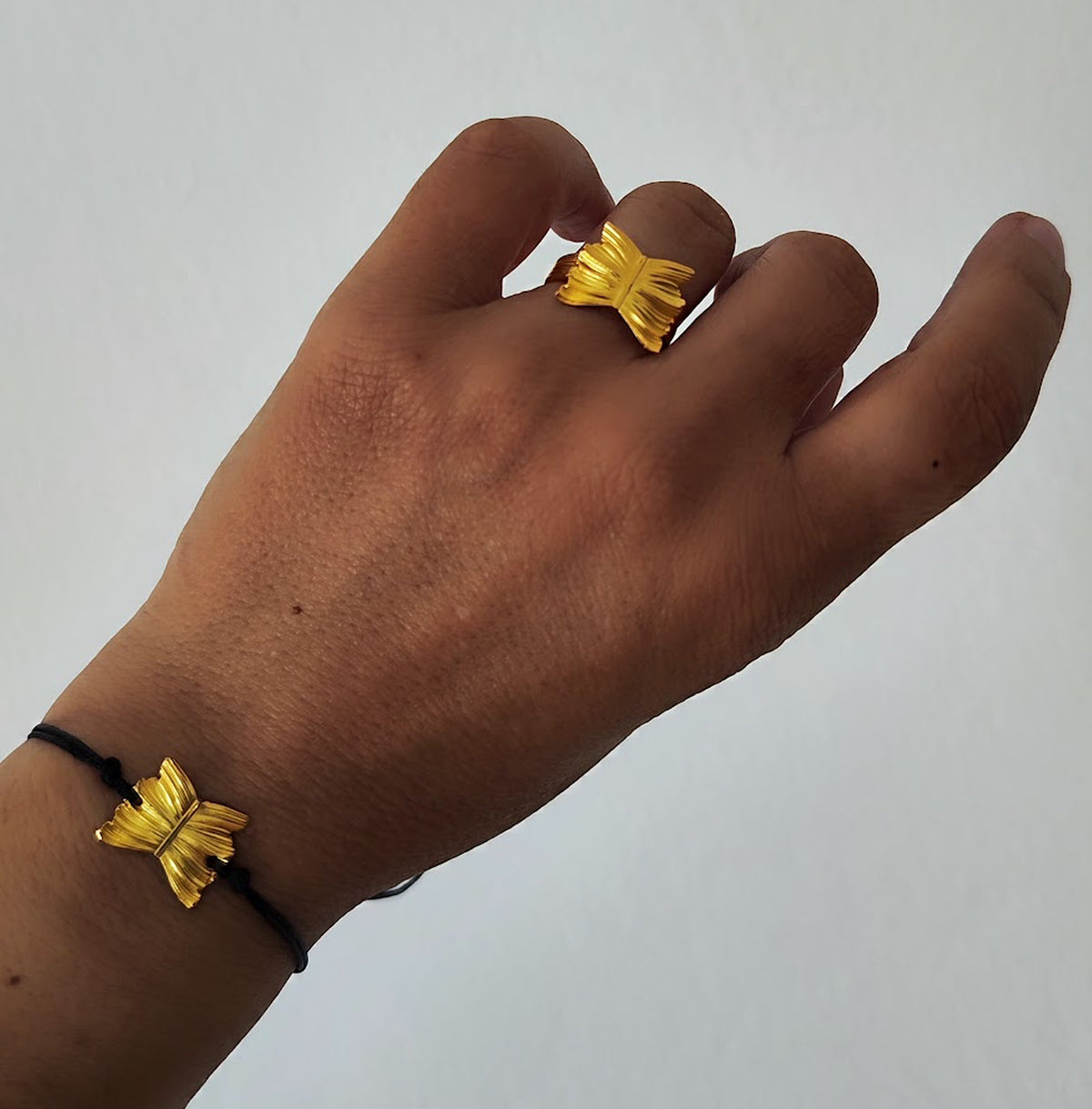 Hand wearing a gold butterfly ring with matching bracelet on a plain background