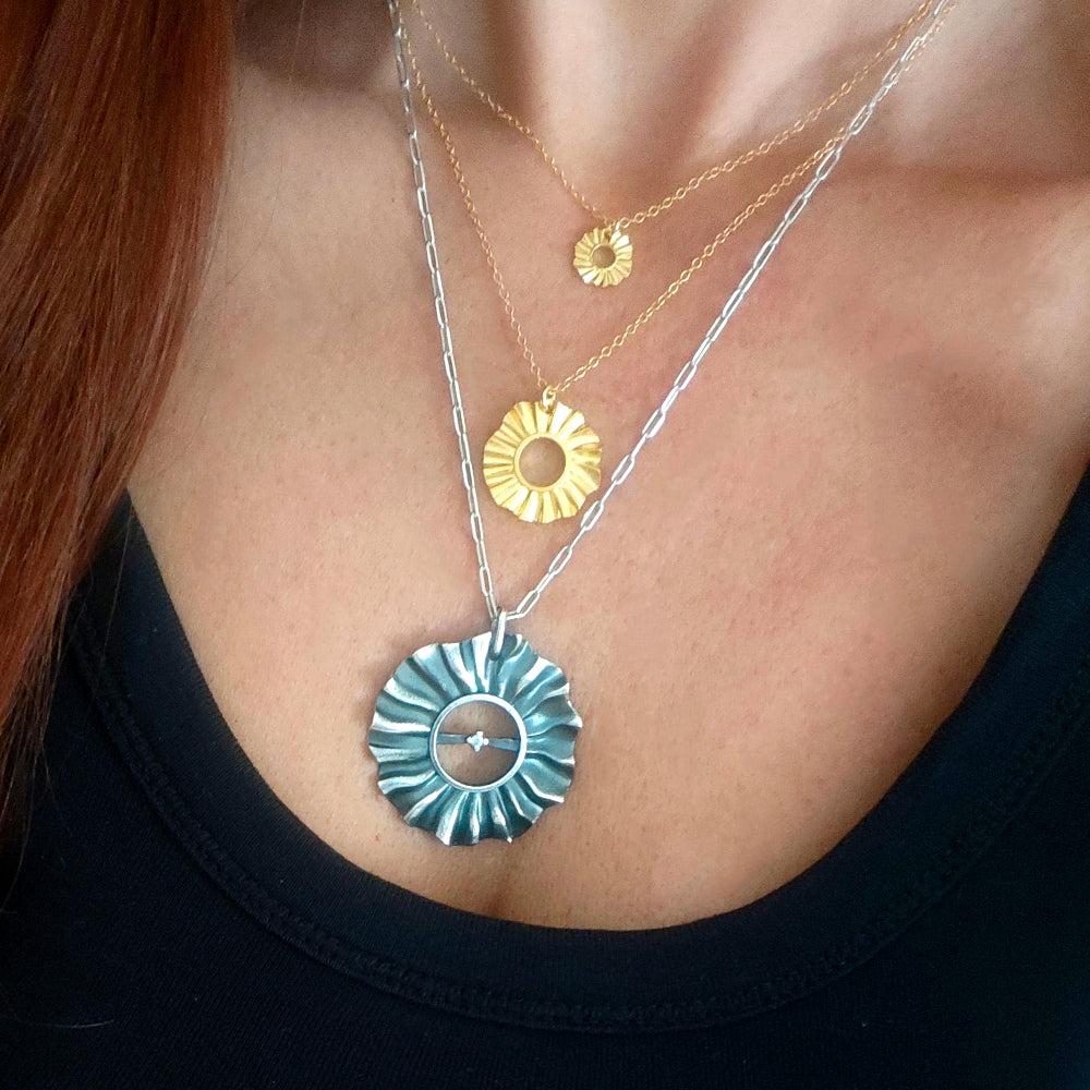 Close-up of a person wearing two necklaces with sun pendants.