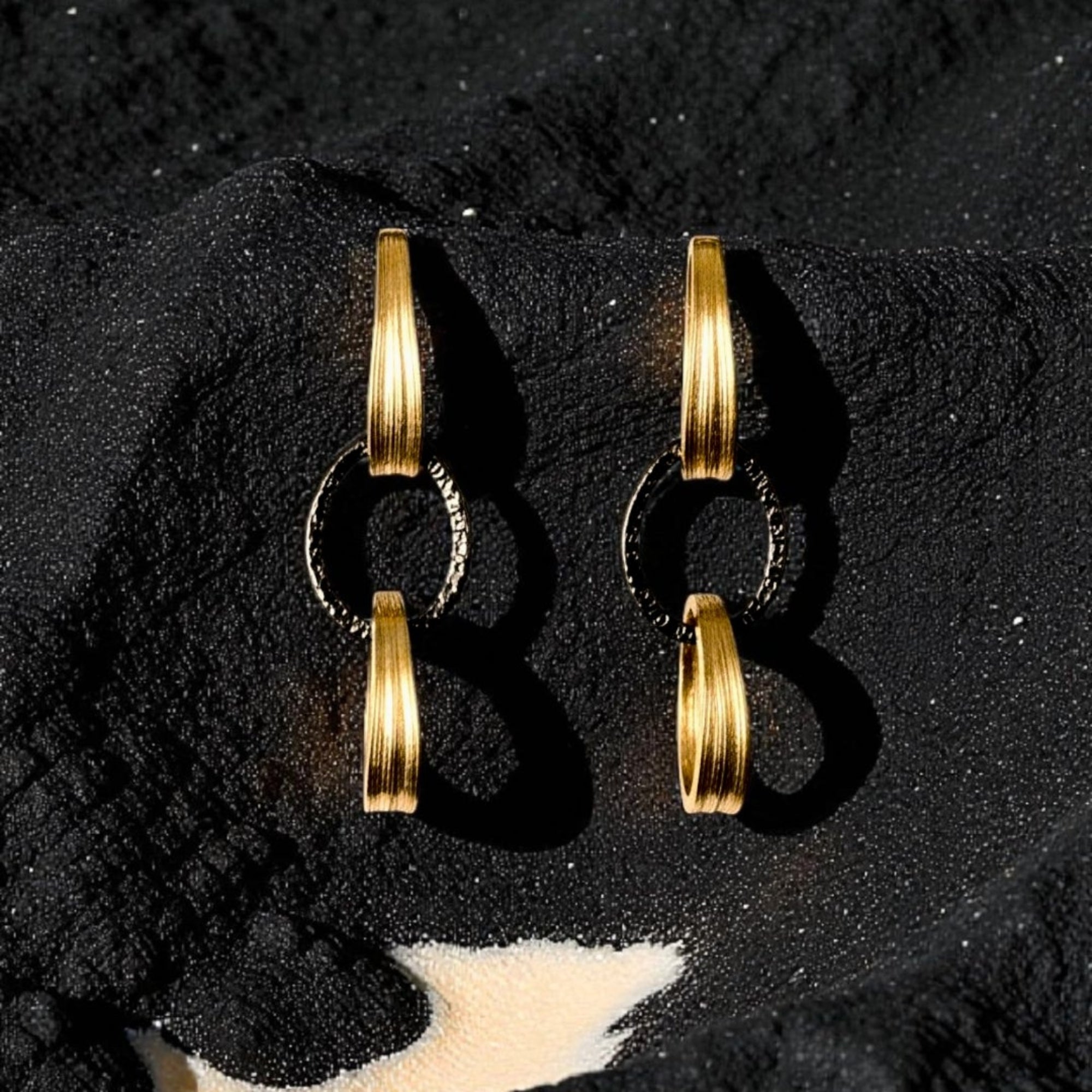 Pair of gold hoop earrings on a textured black surface