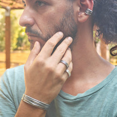 Man with long hair and beard wearing multiple rings and bracelets, outdoors.