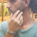 Man with long hair and beard wearing multiple rings and bracelets, outdoors.