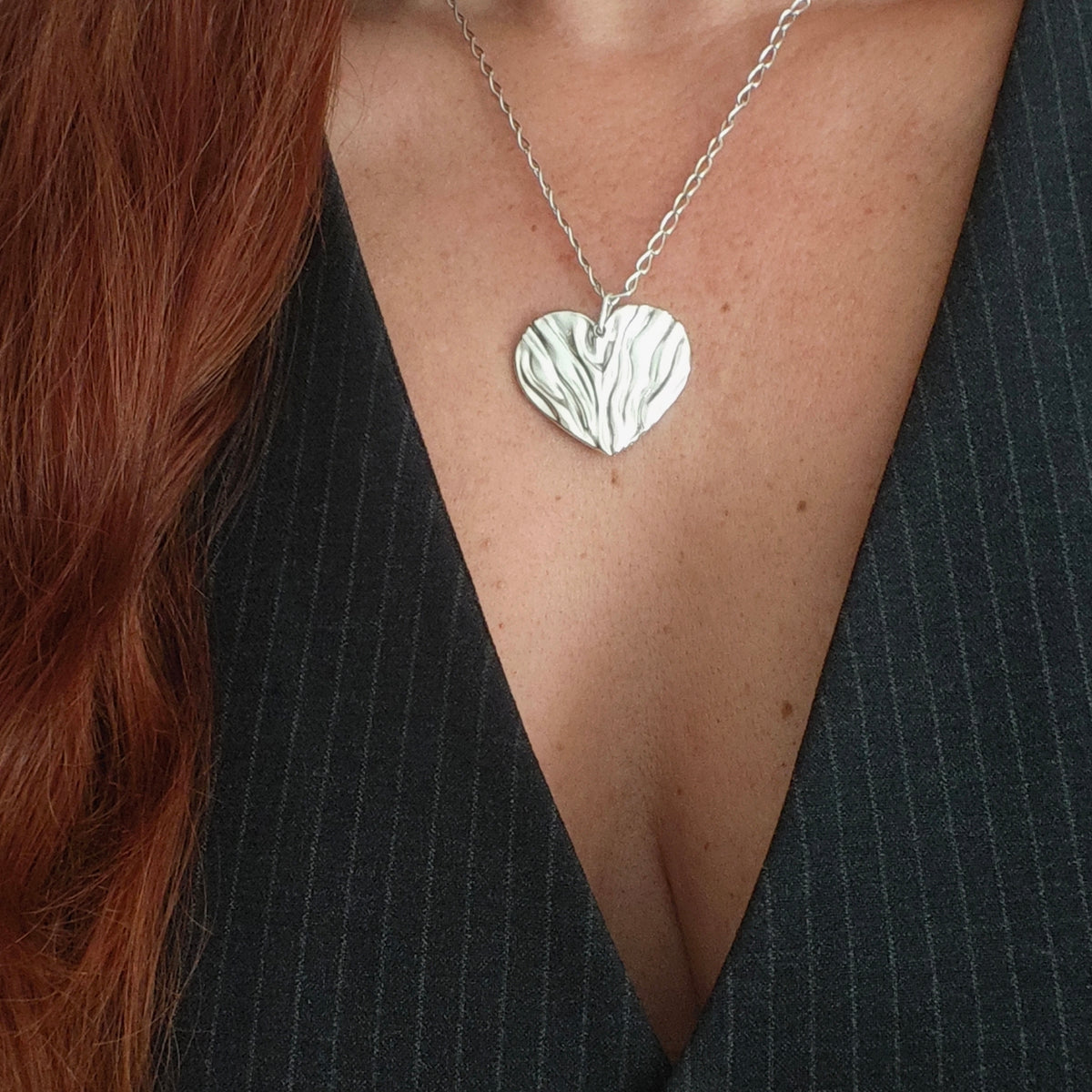 Silver heart-shaped pendant necklace on a person wearing a black top.