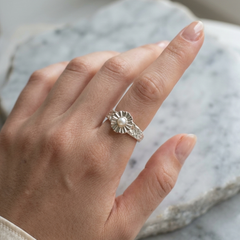 Hand wearing a silver ring with a pearl on a marble surface