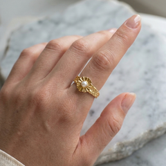 Gold ring with a pearl on a person's finger against a marble background