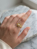 Gold ring with a pearl on a person's finger against a marble background