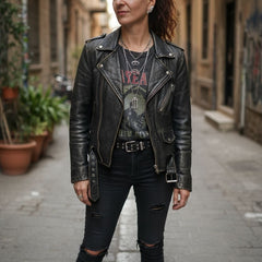 Woman wearing a black leather jacket and ripped jeans standing on a street.
